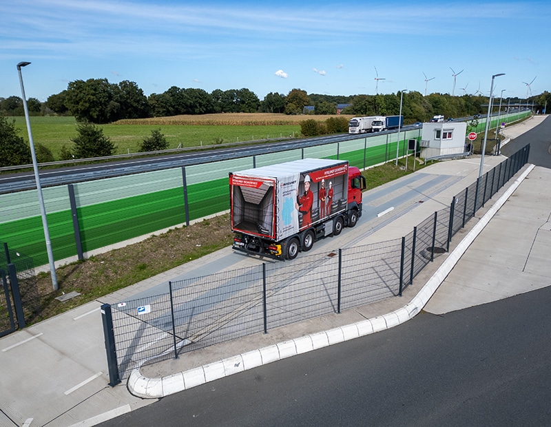 PFREUNDT truck on a road surrounded by fields and wind turbines, with advertising for mobile weighing systems on the tarp.