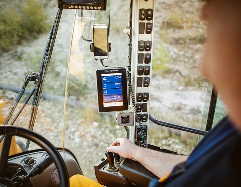 Man operating a mobile excavator with PFREUNDT weighing system, weight display on the screen in the cab.