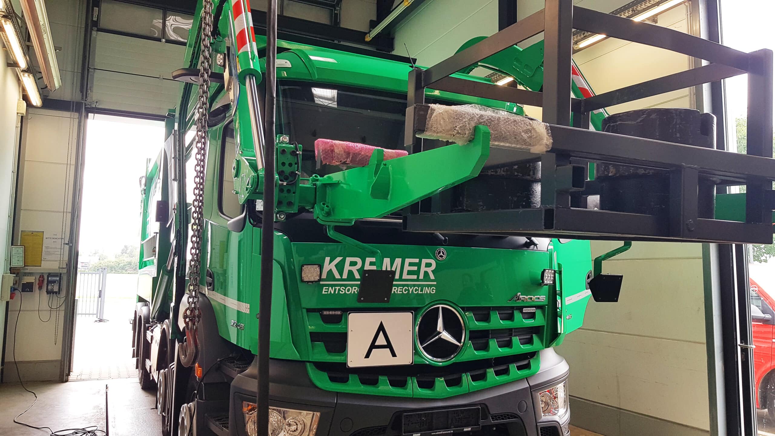 Grüner LKW des Entsorgungsunternehmens Kremer mit Prüfgestell bei der Eichung in einer Werkstatt.