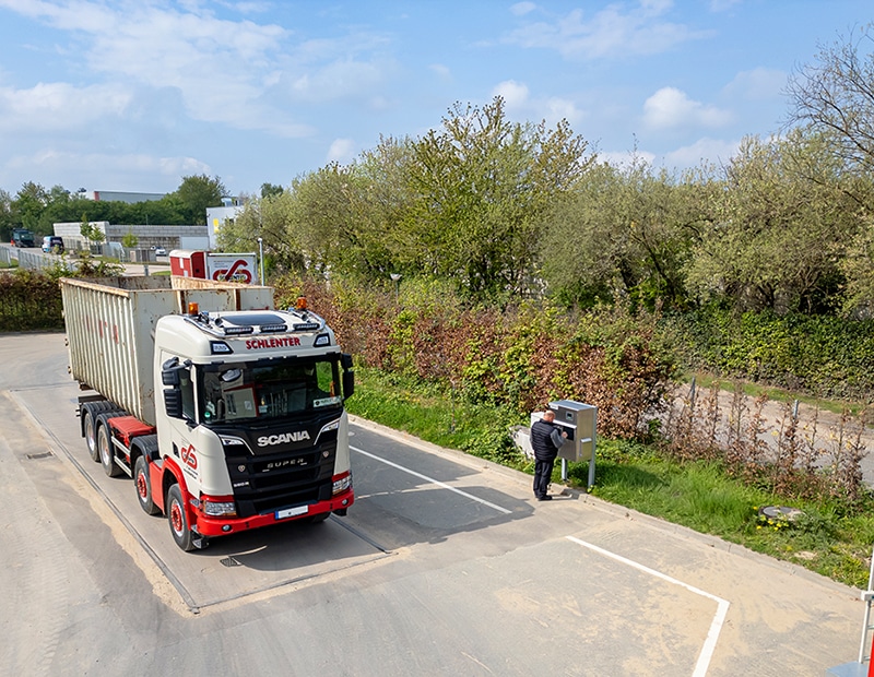 Truck on a mobile PFREUNDT weighing platform, driver using the control unit, spring scenery in the background.