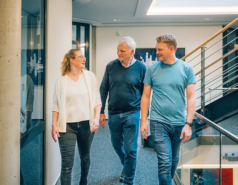 Three people walking and smiling through the PFREUNDT office, provider of mobile weighing systems.