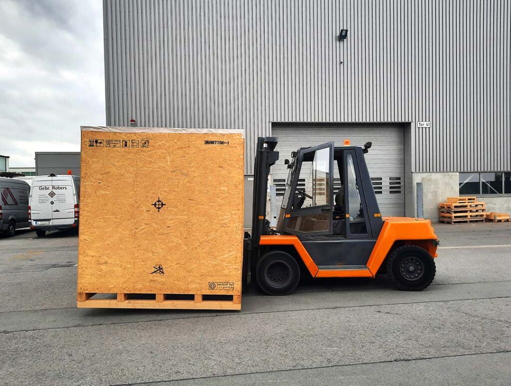 Forklift with PFREUNDT forklift scale transporting a large wooden crate in front of an industrial hall.