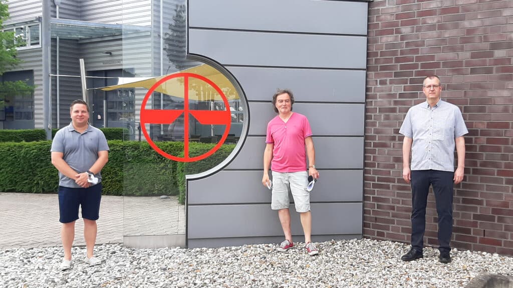 Drei Personen vor dem PFREUNDT-Gebäude mit Firmenlogo, Experten für mobile Wiegesysteme wie Bagger- und Radladerwaagen.