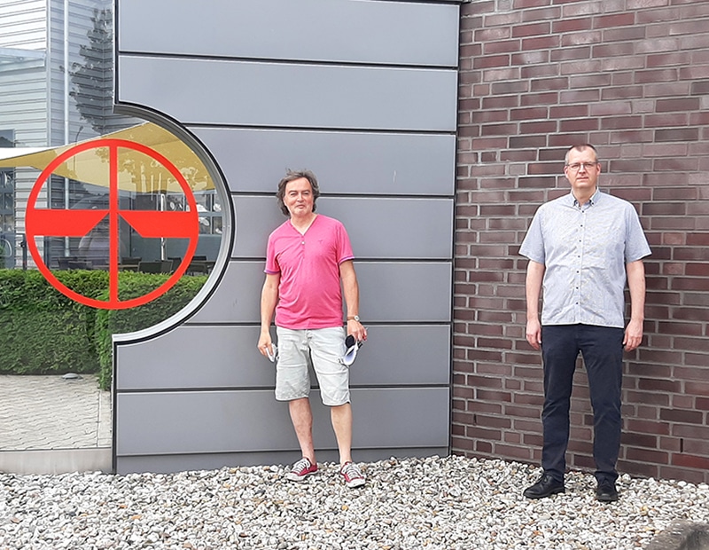 Zwei Personen stehen vor dem Firmenlogo von PFREUNDT, spezialisiert auf mobile Wiegesysteme, an einer modernen Gebäudewand.