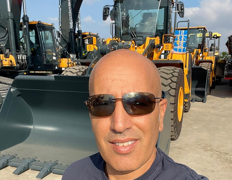 Man wearing sunglasses in front of yellow construction machines that use PFREUNDT mobile weighing systems.