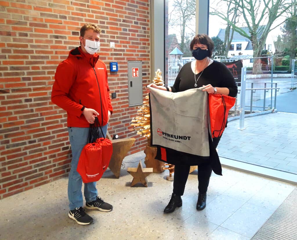 Mitarbeitende von PFREUNDT präsentieren Werbeartikel im Büro, im Hintergrund weihnachtliche Dekorationen.