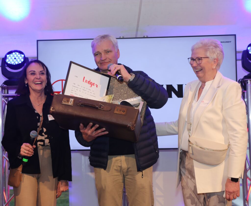 Drei Personen beim Fest zur Firmenübergabe von PFREUNDT; eine Person hält ein Geschenk.