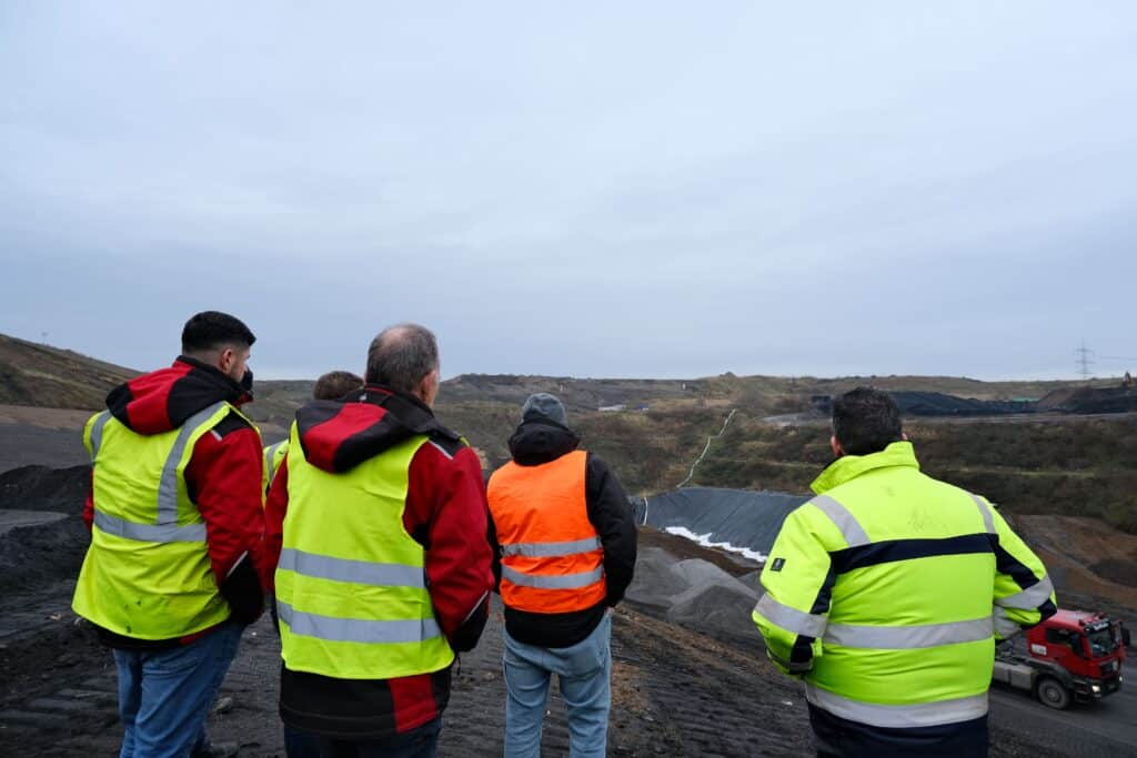 Personen in Warnwesten blicken auf Baustelle, PFREUNDT mobile Wiegesysteme Einsatzort, LKW im Hintergrund.