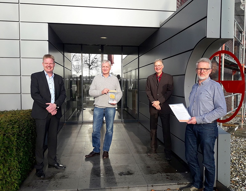 Vier Männer vor Firmengebäude von PFREUNDT, Anbieter mobiler Wiegesysteme, mit Zertifikat und Prototyp in der Hand.