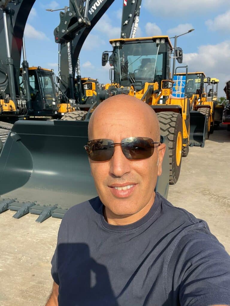 Person wearing sunglasses in front of yellow construction machines, presenting PFREUNDT mobile weighing systems.