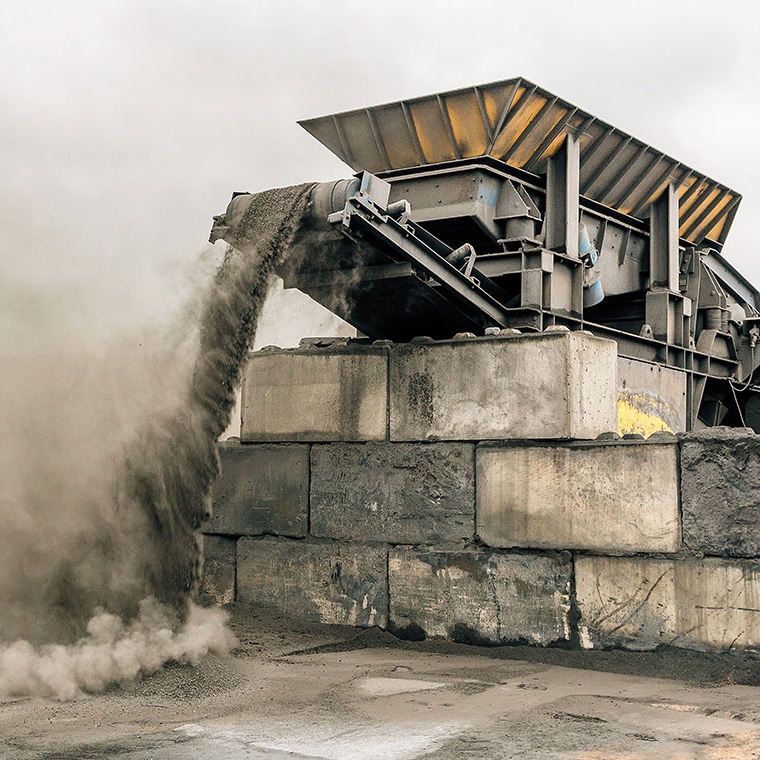 Concasseur mobile équipé de la bascule à bande PFREUNDT déchargeant du matériau dans un environnement poussiéreux.