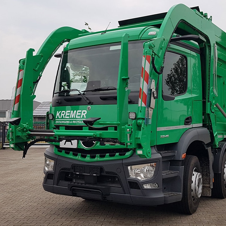 Camion de collecte vert à chargement frontal équipé de la bascule PFREUNDT sur un site d’entreprise.