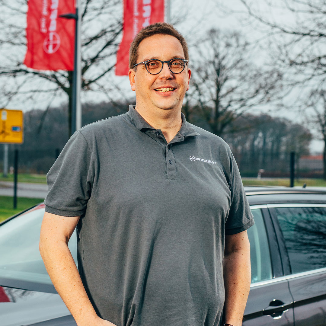 Man in a PFREUNDT polo shirt in front of a car with company flags in the background. Supplier of mobile weighing systems.