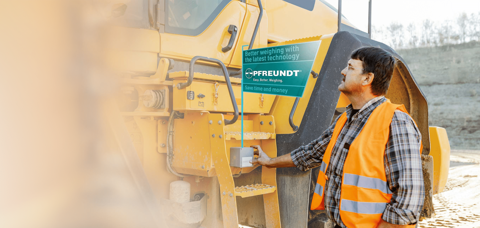 A person standing next to a piece of construction machinery fitted with a PFREUNDT weighing system; sign: ‘Efficient weighing with the latest technology’; outdoors.
