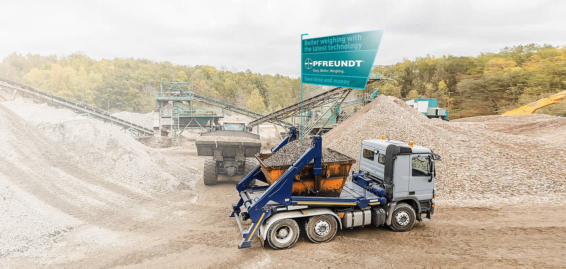A lorry fitted with a PFREUNDT weighing system at a gravel yard, surrounded by conveyor belts and piles of rubble.
