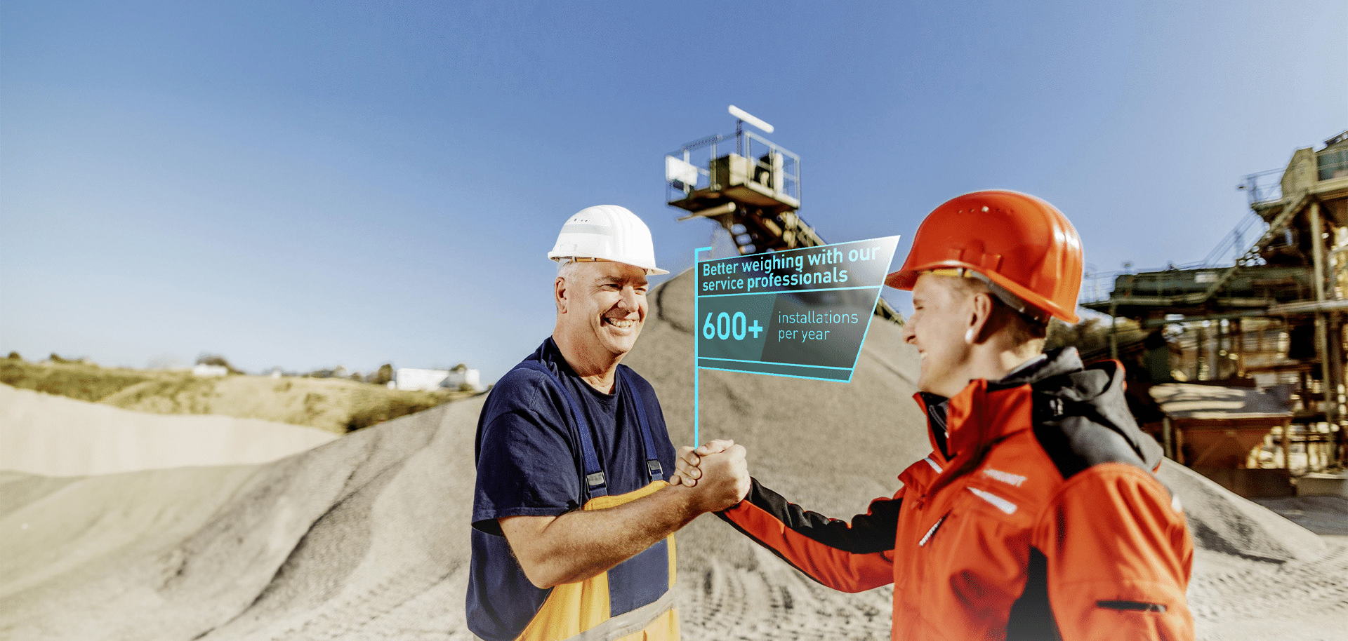 Two men wearing hard hats shake hands in front of construction machinery, with the text highlighting: 600+ installations per year.