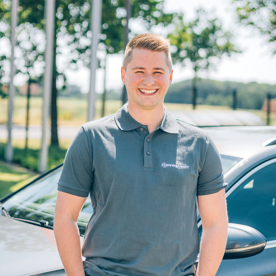 PFREUNDT employee in company clothing smiling in front of a car outdoors.