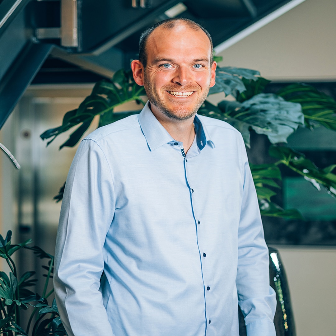 A person in a light-coloured shirt, smiling in front of some plants in the office of PFREUNDT, a supplier of mobile weighing systems.