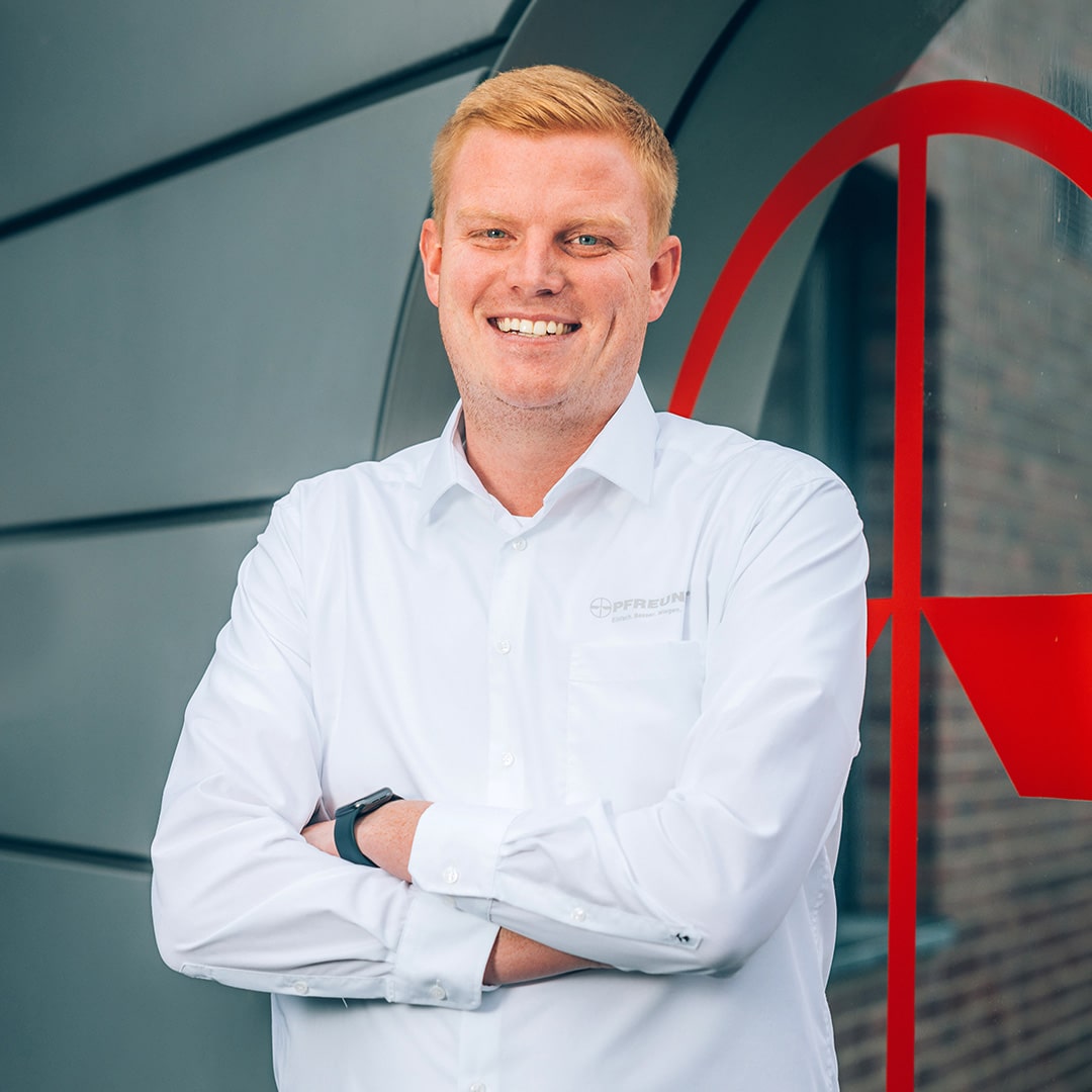 Mann in PFREUNDT-Hemd lächelt vor Firmenlogo. Anbieter mobiler Wiegesysteme wie Bagger- und Kranwaagen.