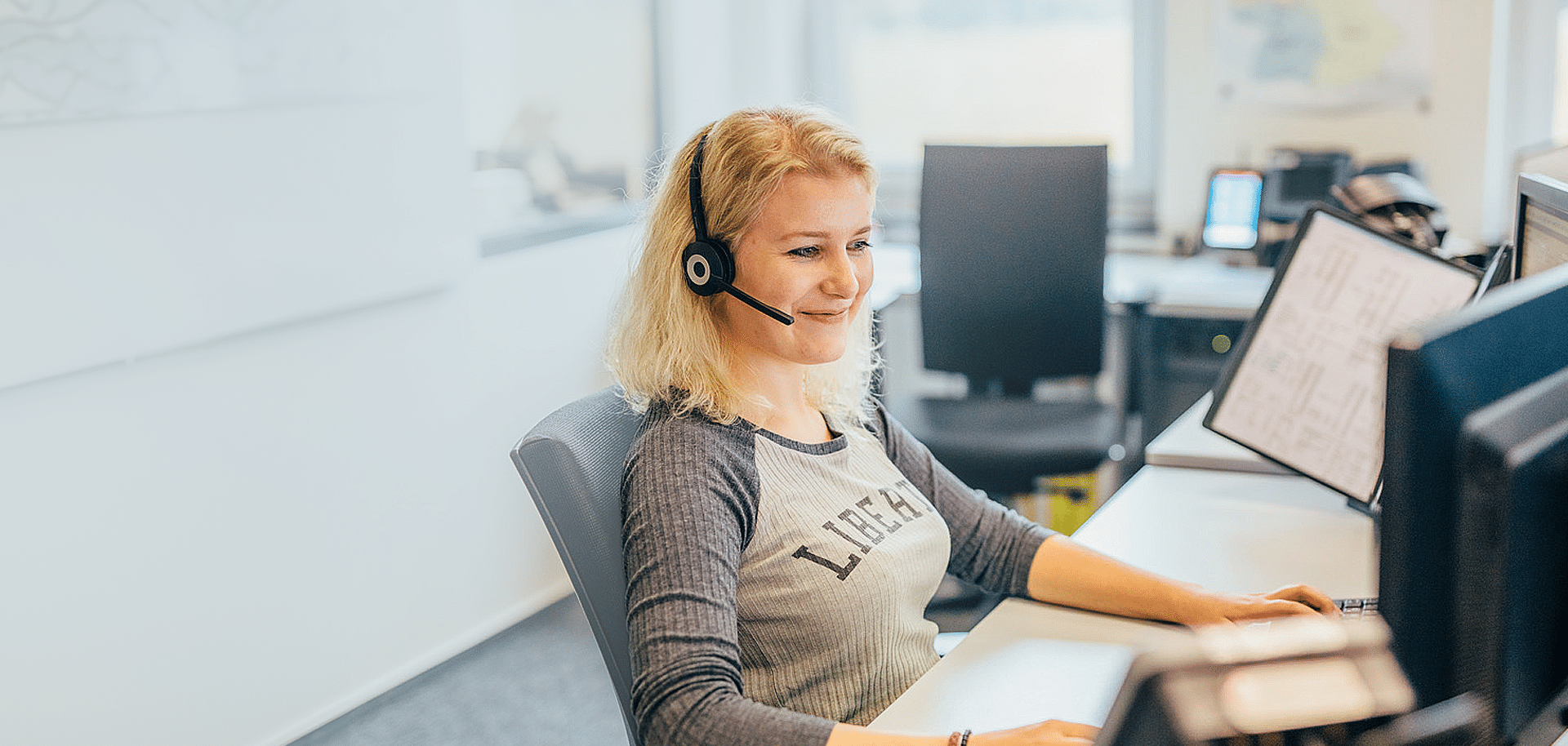 A woman in an office is on the phone using a headset while working on a computer at PFREUNDT, a supplier of mobile weighing systems.